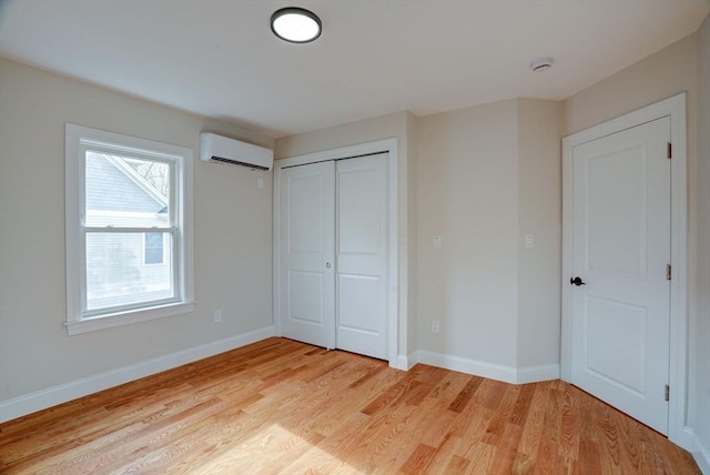 unfurnished bedroom featuring a wall mounted air conditioner, a closet, and light hardwood / wood-style flooring