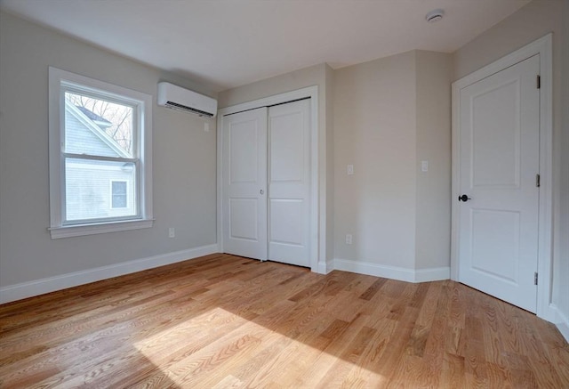 unfurnished bedroom featuring a wall mounted air conditioner, light hardwood / wood-style floors, and a closet