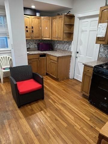 kitchen with decorative backsplash, black range, and light hardwood / wood-style floors