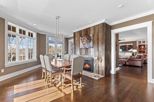 dining room featuring wood finished floors, baseboards, ornamental molding, a glass covered fireplace, and a chandelier