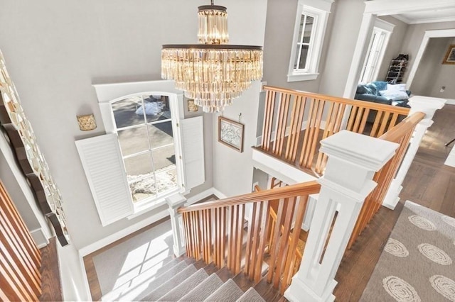 stairway with baseboards, wood finished floors, a chandelier, and ornamental molding