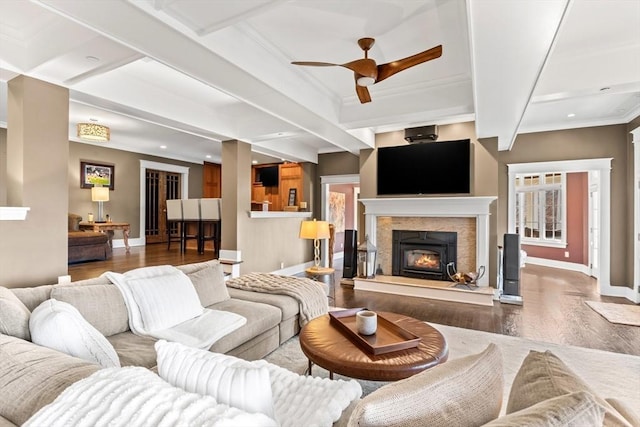 living area featuring beamed ceiling, wood finished floors, a lit fireplace, crown molding, and baseboards