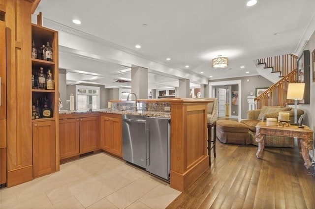 kitchen with light stone counters, brown cabinetry, a sink, crown molding, and open floor plan