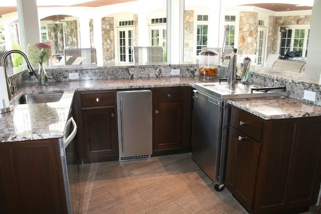 kitchen with a sink, light stone counters, dark brown cabinetry, and refrigerator