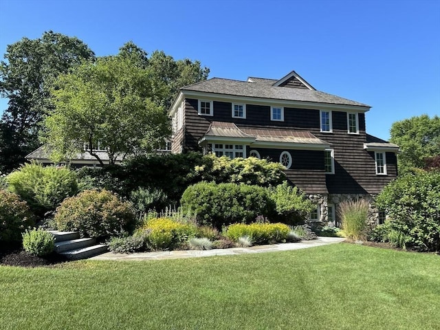 view of front of house featuring a standing seam roof, a front lawn, stone siding, and metal roof