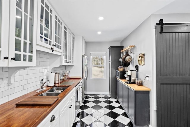 kitchen with stainless steel appliances, wooden counters, glass insert cabinets, a sink, and tile patterned floors