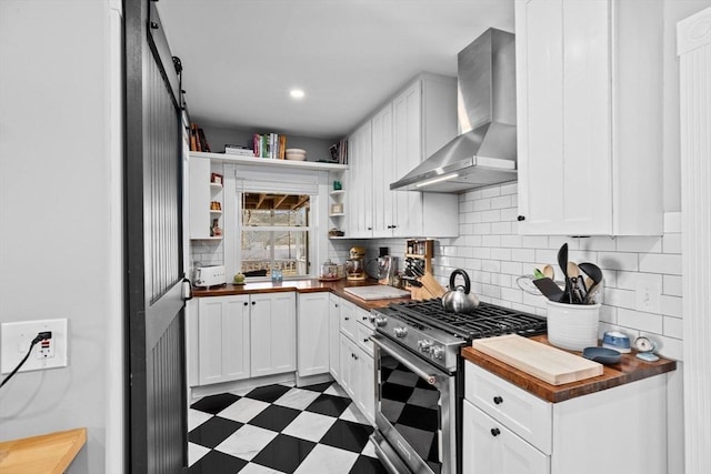 kitchen with light floors, butcher block countertops, wall chimney range hood, and stainless steel gas range oven