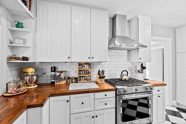 kitchen with butcher block counters, white cabinetry, stainless steel gas range oven, and wall chimney range hood