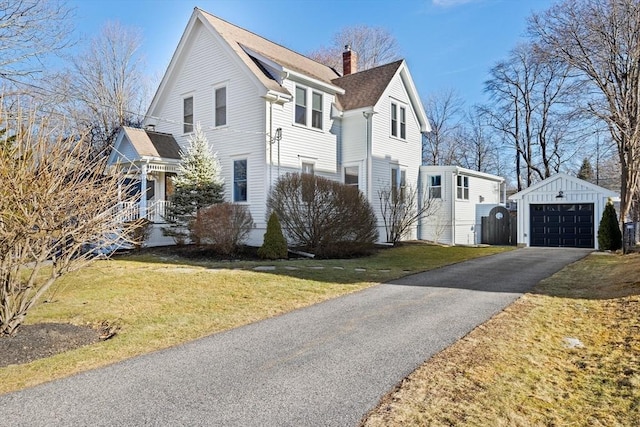 view of side of property featuring an outbuilding, a detached garage, driveway, a yard, and a chimney