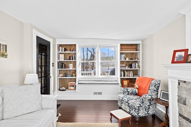 living area with visible vents, baseboards, wood-type flooring, a stone fireplace, and built in shelves