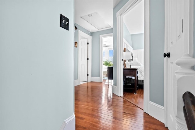 corridor with hardwood / wood-style floors, attic access, and baseboards