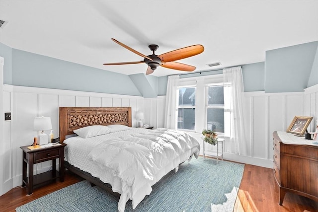 bedroom with a wainscoted wall, a ceiling fan, visible vents, and wood finished floors