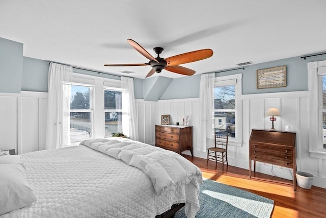 bedroom featuring multiple windows, wainscoting, wood finished floors, and visible vents