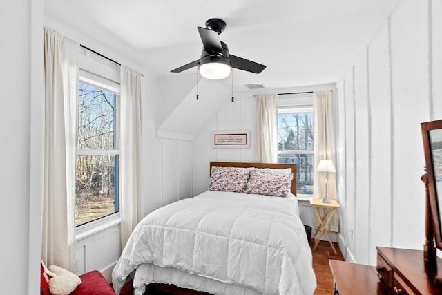 bedroom featuring multiple windows, wood finished floors, and a decorative wall