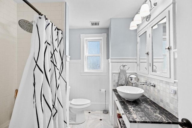 full bathroom with marble finish floor, visible vents, toilet, wainscoting, and a tile shower