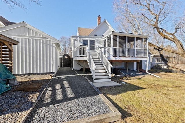 back of property featuring a sunroom, a lawn, stairway, a gate, and a chimney