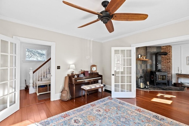 living area with baseboards, stairway, hardwood / wood-style floors, a wood stove, and crown molding