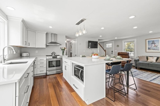 kitchen featuring stainless steel appliances, a sink, wall chimney exhaust hood, open floor plan, and a breakfast bar