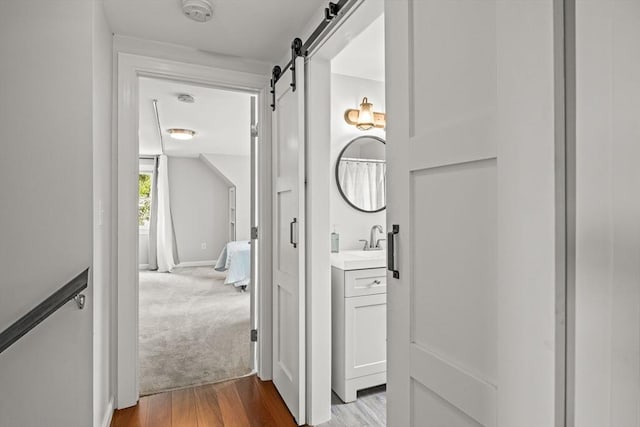 hall with a barn door, a sink, wood finished floors, carpet flooring, and baseboards