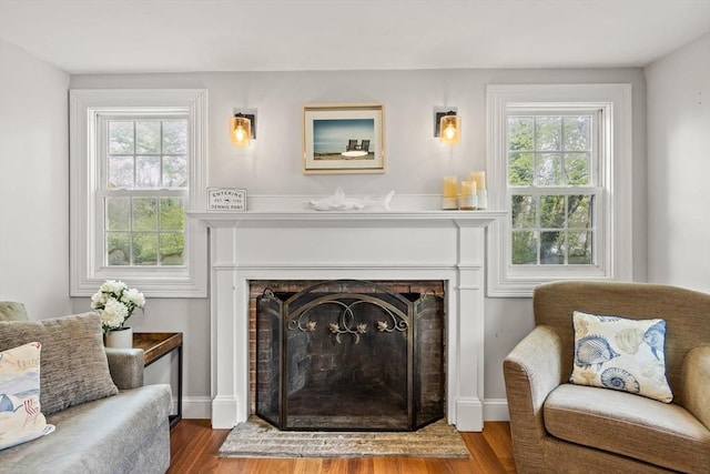 sitting room featuring wood finished floors, healthy amount of natural light, and a fireplace with raised hearth