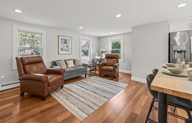 living area featuring healthy amount of natural light, recessed lighting, light wood-style floors, baseboards, and a baseboard heating unit