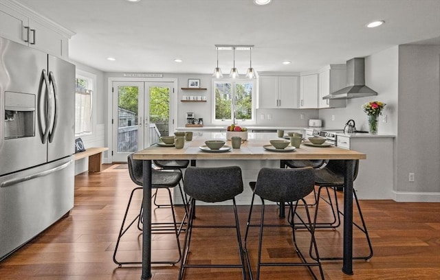 kitchen with stainless steel appliances, wall chimney exhaust hood, light countertops, white cabinetry, and dark wood-style flooring