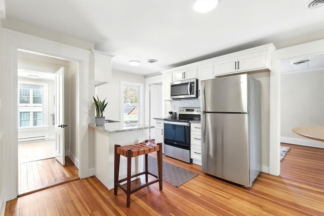 kitchen with light wood-type flooring, visible vents, appliances with stainless steel finishes, white cabinets, and decorative backsplash
