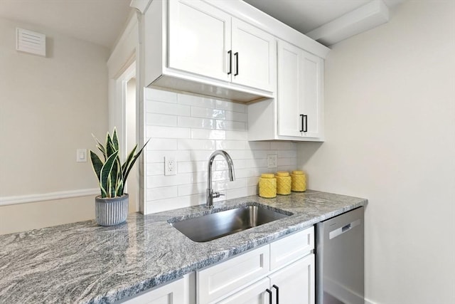 kitchen featuring light stone counters, a sink, white cabinets, stainless steel dishwasher, and backsplash