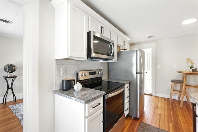 kitchen with baseboards, white cabinets, appliances with stainless steel finishes, light wood-type flooring, and backsplash