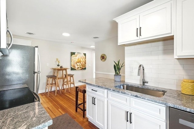 kitchen featuring a sink, backsplash, wood finished floors, white cabinetry, and stainless steel appliances