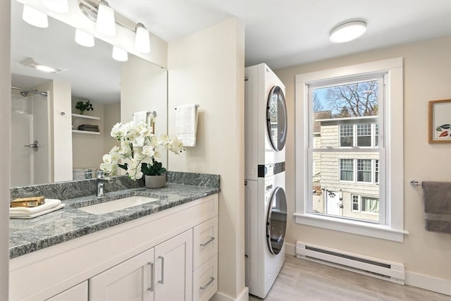 laundry area featuring baseboards, laundry area, a sink, stacked washer and dryer, and baseboard heating