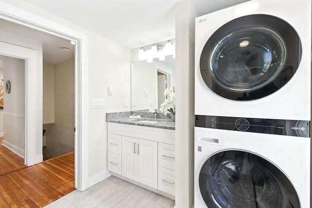 washroom featuring light wood finished floors, baseboards, laundry area, stacked washing maching and dryer, and a sink