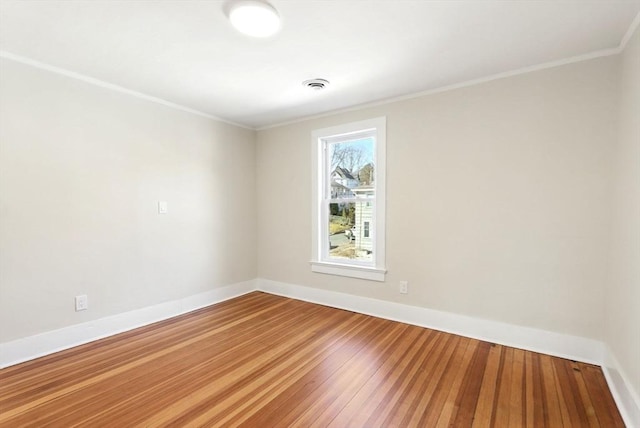spare room featuring visible vents, baseboards, hardwood / wood-style floors, and crown molding