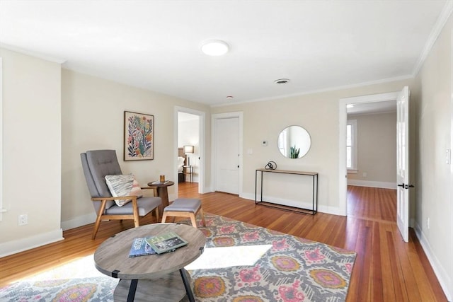 living area with visible vents, baseboards, wood finished floors, and ornamental molding