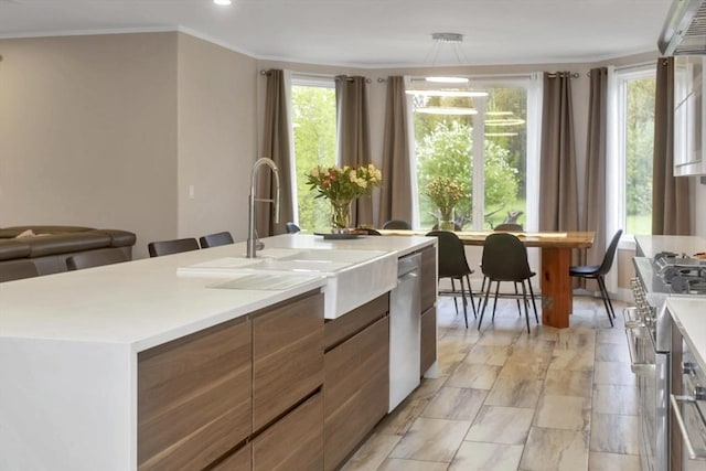 kitchen with appliances with stainless steel finishes, a sink, light countertops, modern cabinets, and a center island with sink
