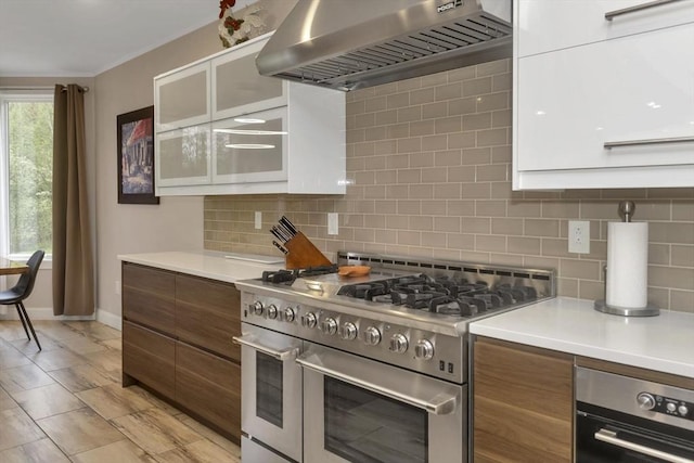kitchen featuring double oven range, range hood, baseboards, light countertops, and decorative backsplash