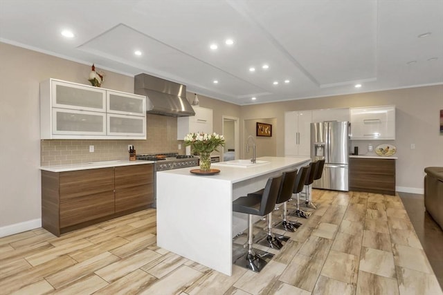 kitchen with stainless steel appliances, a sink, wall chimney range hood, light countertops, and decorative backsplash
