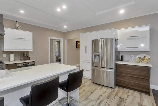 kitchen with stainless steel fridge with ice dispenser, modern cabinets, a kitchen bar, white cabinets, and recessed lighting