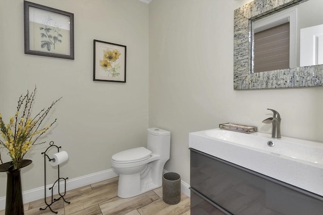 bathroom featuring toilet, baseboards, wood finished floors, and vanity