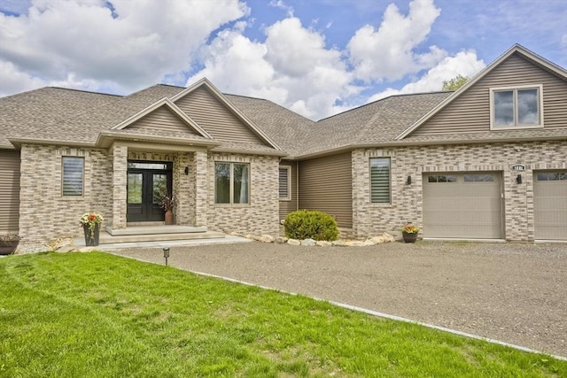 view of front facade with french doors, brick siding, driveway, a front yard, and a garage