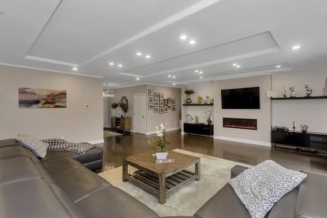 living room featuring recessed lighting, wood finished floors, baseboards, a glass covered fireplace, and a raised ceiling