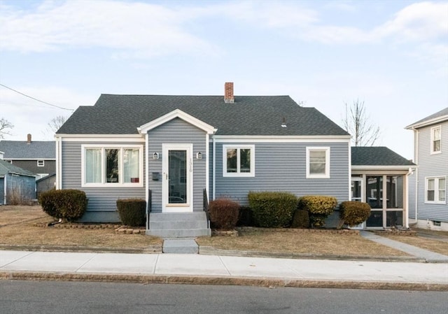 view of front of property with roof with shingles, a chimney, and a sunroom