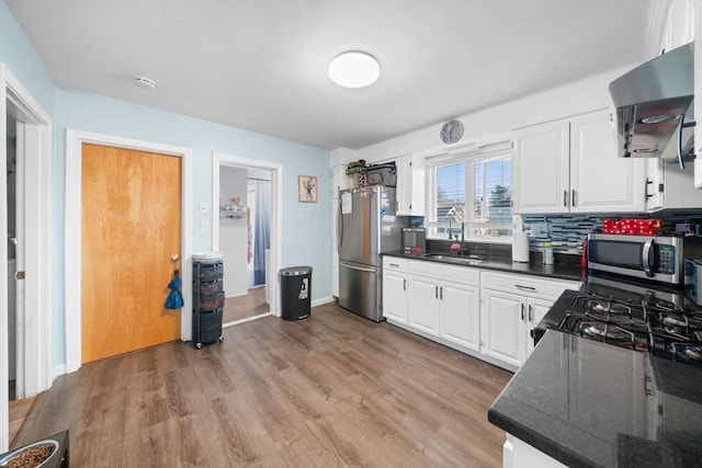 kitchen with stainless steel appliances, a sink, white cabinets, wall chimney range hood, and light wood-type flooring