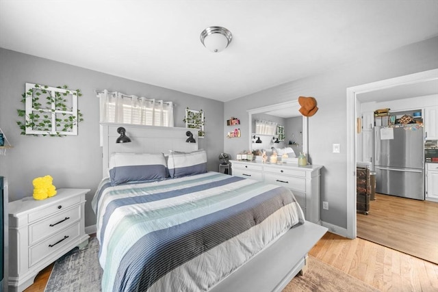 bedroom featuring light wood-type flooring, freestanding refrigerator, and baseboards