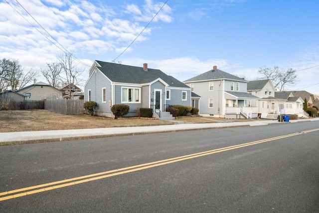 view of front of home with a chimney, a residential view, fence, and roof with shingles