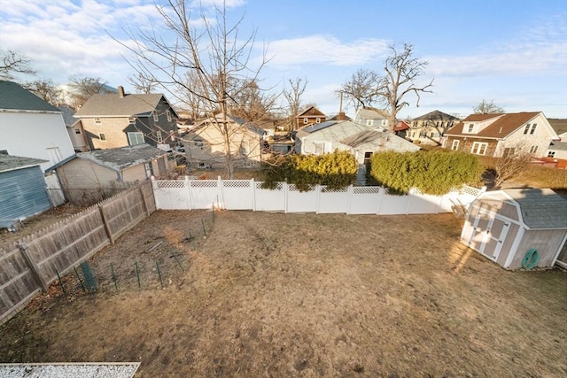 view of yard with a shed, an outdoor structure, a fenced backyard, and a residential view