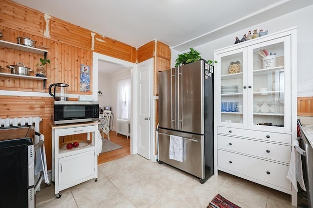 kitchen featuring stainless steel appliances, wooden walls, radiator, and white cabinets