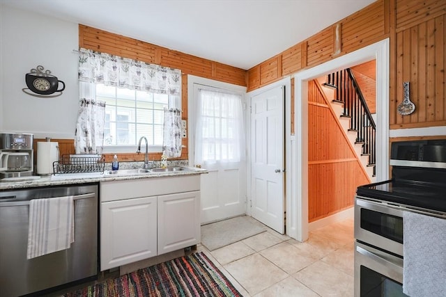 kitchen featuring sink, wooden walls, white cabinets, and appliances with stainless steel finishes