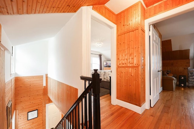 corridor featuring light hardwood / wood-style flooring, wooden walls, and lofted ceiling