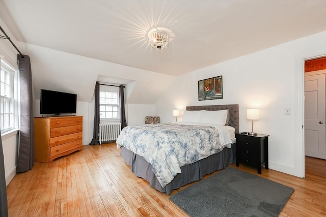 bedroom featuring light wood-type flooring, vaulted ceiling, and radiator